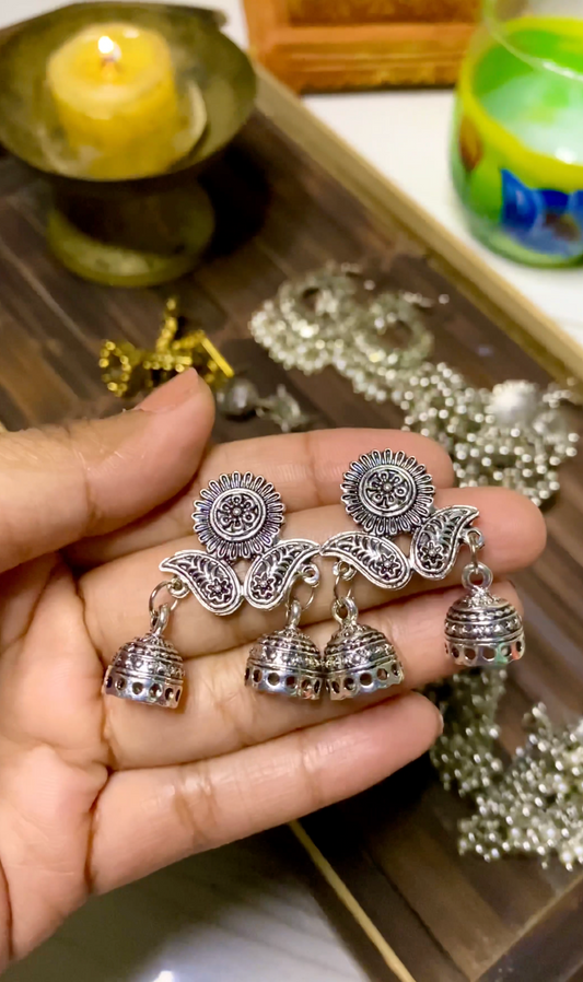 Silver earrings held in a hand with a blurred background of jewelry and a candle.